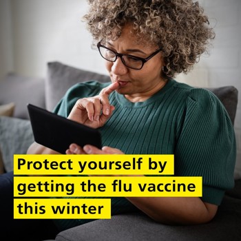 A woman with curly hair and glasses sits on a couch, reading a tablet. She looks focused. Text overlay: "Protect yourself by getting the flu vaccine this winter."
