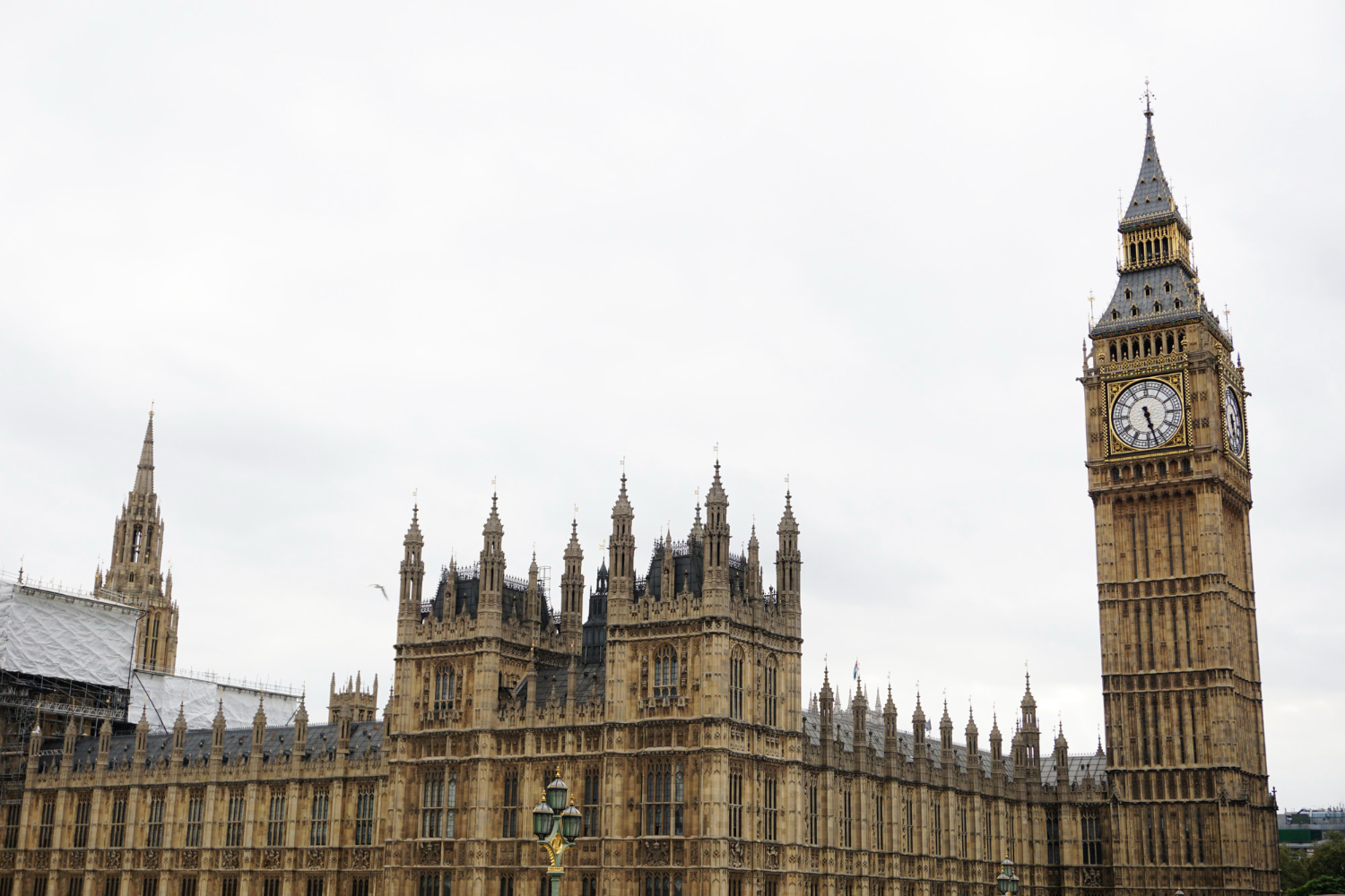 Gothic-style Palace of Westminster with Big Ben clock tower under a cloudy sky. 