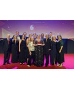 A group of people on stage at an award show. The person is the middle is holding an award.