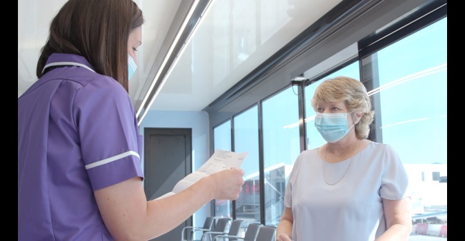 A healthcare professional ready a piece of paper to a women who is wearing a face mask